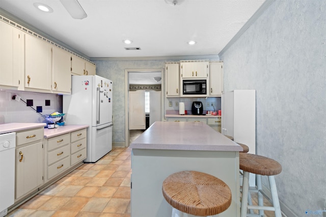 kitchen featuring a kitchen bar, tasteful backsplash, white appliances, cream cabinetry, and a kitchen island