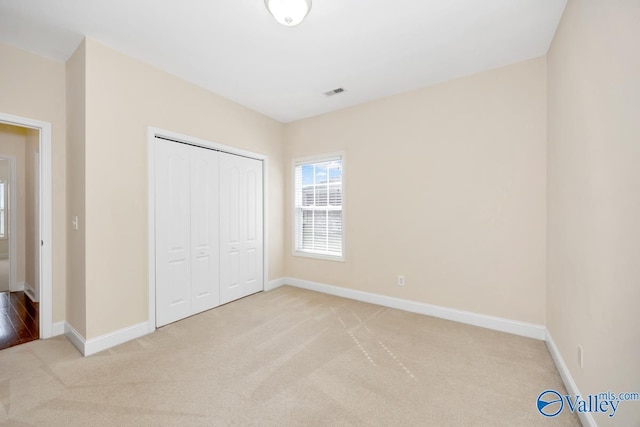 unfurnished bedroom featuring a closet, light colored carpet, baseboards, and visible vents