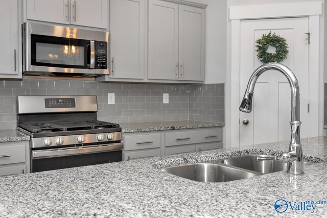 kitchen with backsplash, sink, stainless steel appliances, and light stone counters