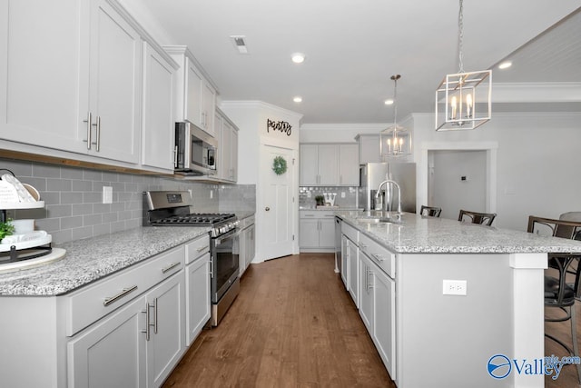 kitchen with decorative backsplash, hardwood / wood-style floors, a kitchen bar, appliances with stainless steel finishes, and a center island with sink