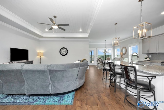 living room featuring ceiling fan with notable chandelier, hardwood / wood-style floors, a tray ceiling, ornamental molding, and sink