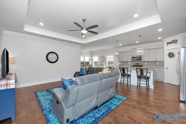 living room with a tray ceiling, ceiling fan, crown molding, and dark hardwood / wood-style floors