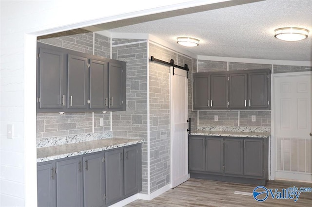 kitchen with a barn door, tasteful backsplash, light stone countertops, a textured ceiling, and light wood-type flooring