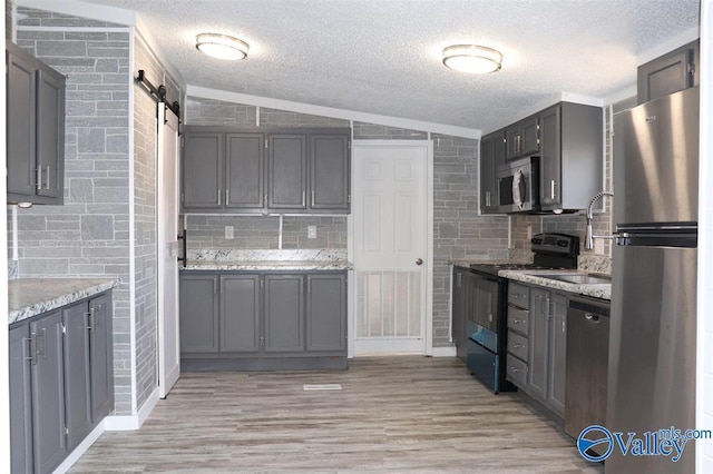 kitchen featuring light wood finished floors, backsplash, a barn door, appliances with stainless steel finishes, and vaulted ceiling