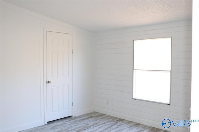 unfurnished room with light wood-style flooring, a textured ceiling, and wooden walls