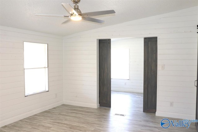 spare room featuring lofted ceiling, light wood-style flooring, wooden walls, and a textured ceiling