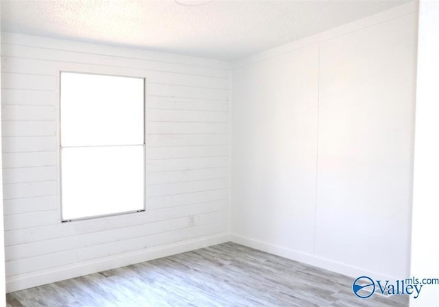 spare room featuring wooden walls, a textured ceiling, and wood finished floors