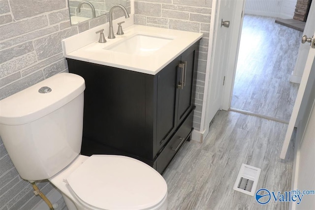 half bathroom with visible vents, toilet, wood finished floors, vanity, and tile walls