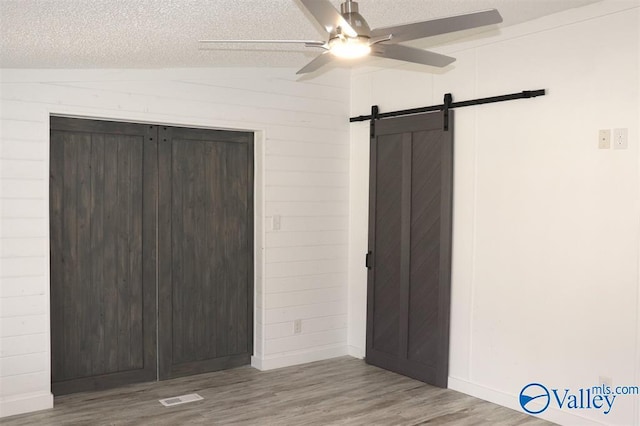 unfurnished bedroom featuring lofted ceiling, visible vents, a barn door, a textured ceiling, and wood finished floors