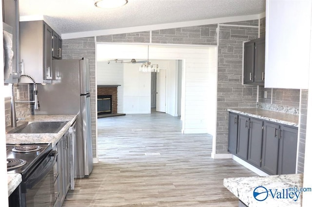 kitchen featuring black electric range oven, backsplash, a brick fireplace, a textured ceiling, and light wood-type flooring