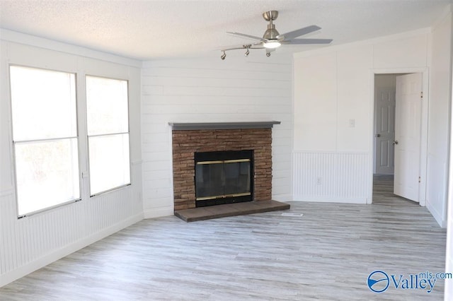 unfurnished living room featuring a brick fireplace, ceiling fan, a textured ceiling, and wood finished floors