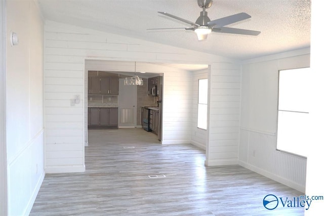 empty room featuring ceiling fan, a textured ceiling, a healthy amount of sunlight, vaulted ceiling, and light wood finished floors