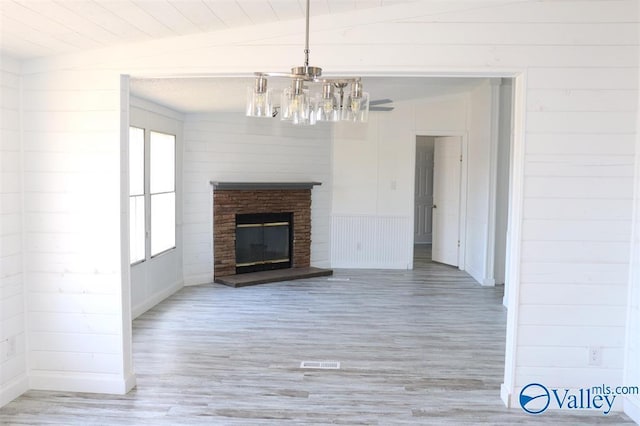 unfurnished living room with lofted ceiling, a brick fireplace, light wood-style flooring, and a notable chandelier