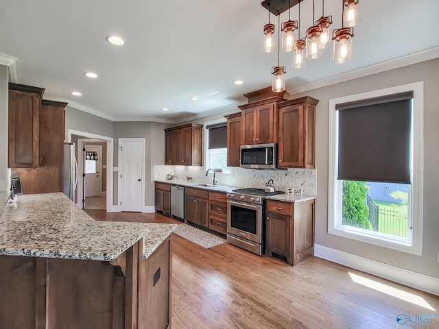 kitchen with appliances with stainless steel finishes, decorative light fixtures, decorative backsplash, light stone counters, and crown molding