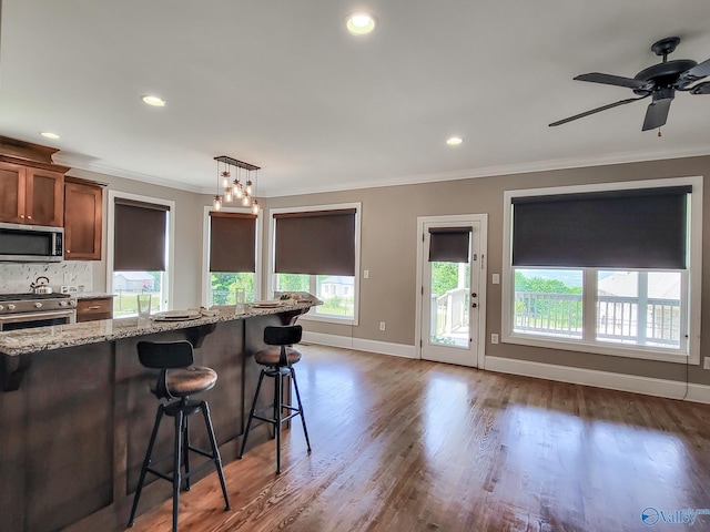 kitchen featuring pendant lighting, appliances with stainless steel finishes, ornamental molding, light stone countertops, and a kitchen bar