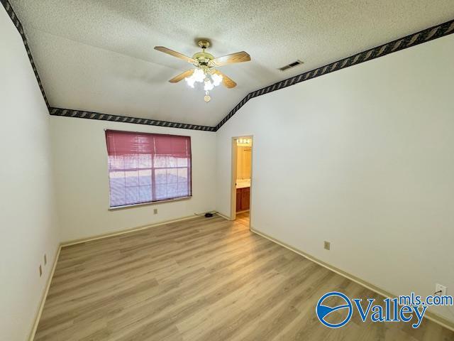 empty room with ceiling fan, light wood-type flooring, a textured ceiling, and vaulted ceiling