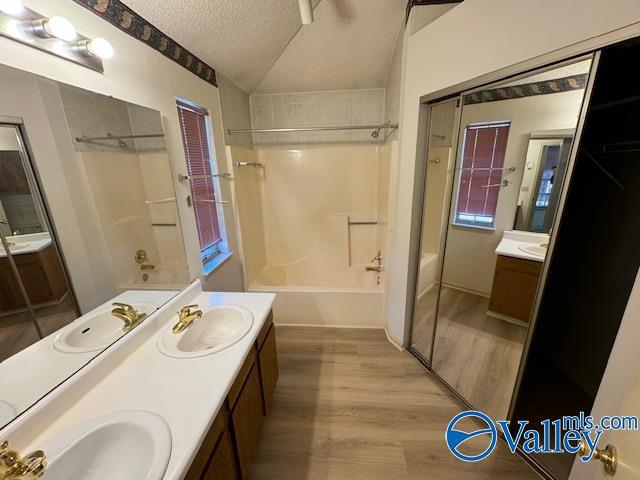 bathroom with vanity, lofted ceiling, hardwood / wood-style flooring, a textured ceiling, and shower / bathtub combination