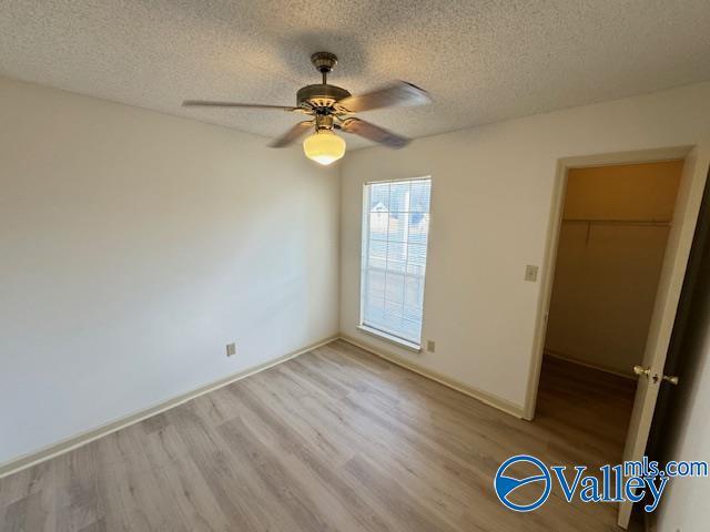 unfurnished bedroom with a walk in closet, a textured ceiling, ceiling fan, light hardwood / wood-style floors, and a closet