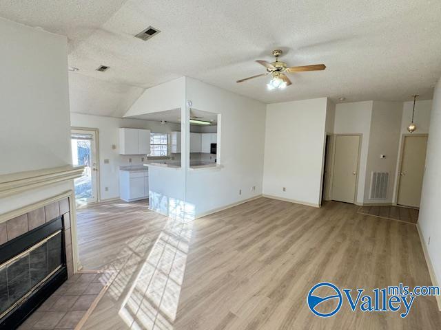 unfurnished living room with a tile fireplace, light hardwood / wood-style flooring, vaulted ceiling, ceiling fan, and a textured ceiling