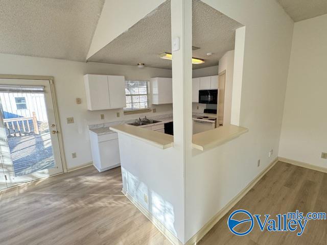 kitchen featuring kitchen peninsula, a textured ceiling, white range with electric stovetop, vaulted ceiling, and white cabinetry