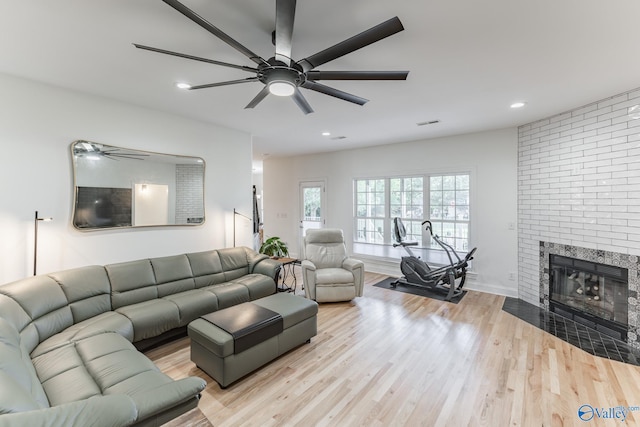 living room with a brick fireplace, light hardwood / wood-style flooring, and ceiling fan