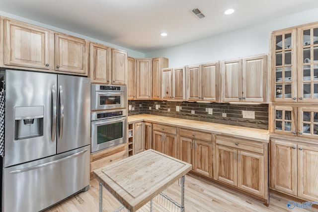 kitchen with appliances with stainless steel finishes, light brown cabinets, light hardwood / wood-style floors, and backsplash