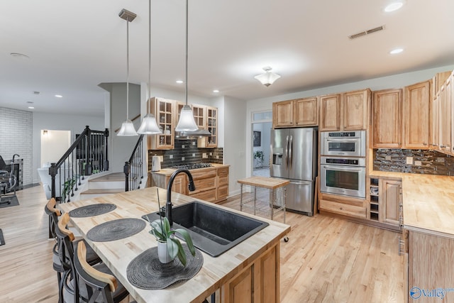 kitchen featuring light wood-type flooring, tasteful backsplash, sink, stainless steel appliances, and hanging light fixtures