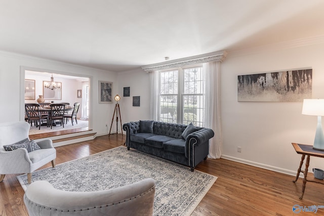 living room featuring baseboards, ornamental molding, a chandelier, and wood finished floors