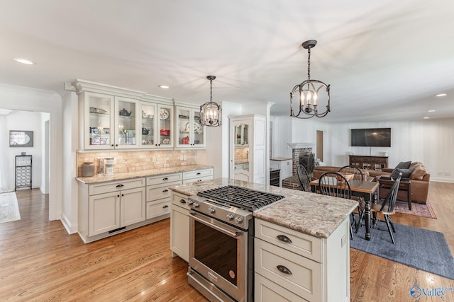 kitchen featuring pendant lighting, tasteful backsplash, a stone fireplace, light wood-type flooring, and high end stove