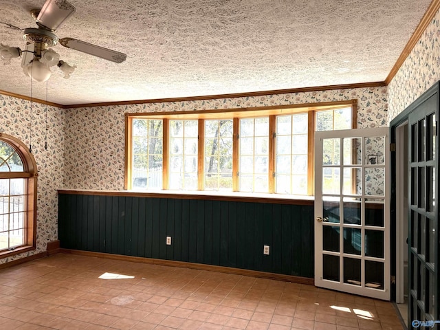 tiled empty room with wallpapered walls, ornamental molding, a wealth of natural light, and a textured ceiling