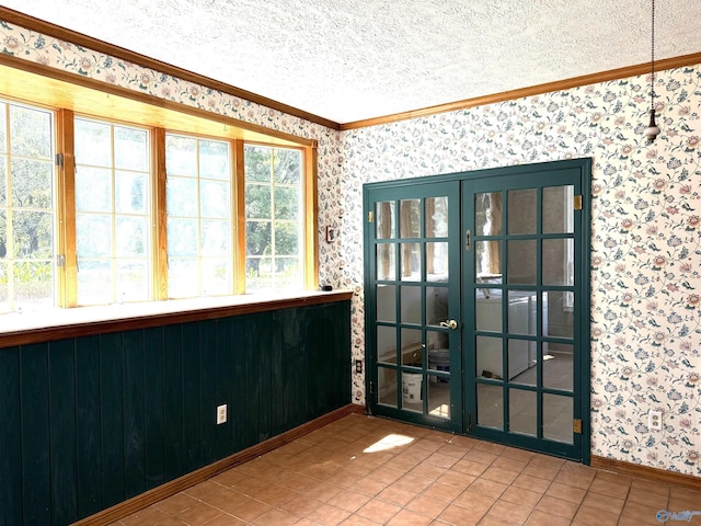 tiled spare room featuring french doors, crown molding, a textured ceiling, baseboards, and wallpapered walls