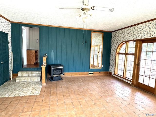 tiled spare room with visible vents, ornamental molding, a wood stove, and a ceiling fan