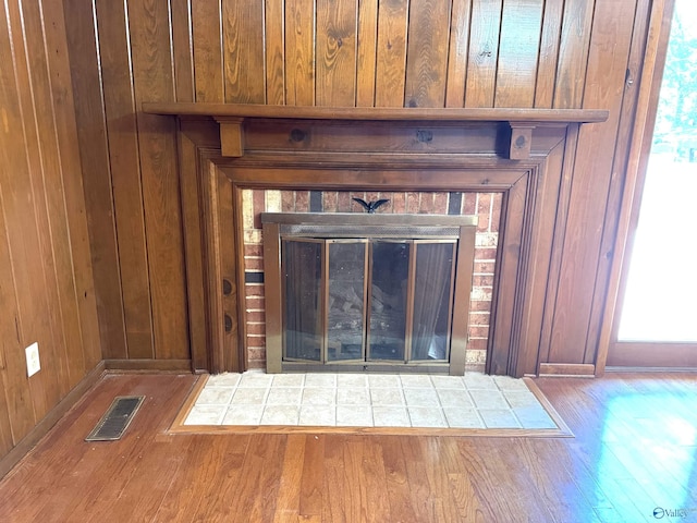 room details featuring a brick fireplace, visible vents, wooden walls, and wood finished floors