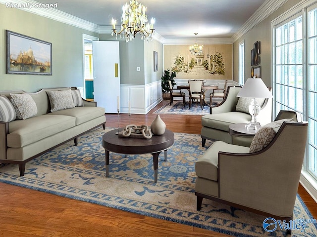 living room with a wainscoted wall, a notable chandelier, a decorative wall, ornamental molding, and wood finished floors