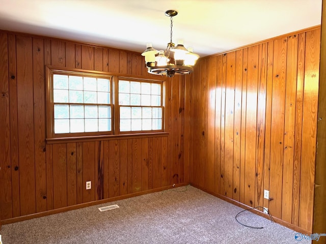 carpeted empty room with baseboards, wooden walls, visible vents, and a notable chandelier