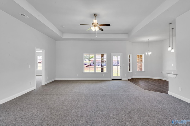 unfurnished living room featuring a wealth of natural light, visible vents, a tray ceiling, carpet floors, and baseboards