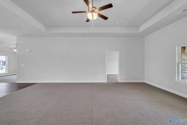 empty room with a tray ceiling, baseboards, visible vents, and dark colored carpet