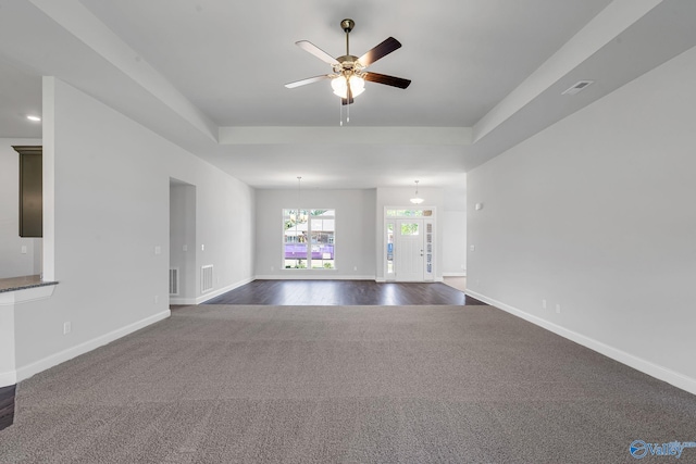 unfurnished living room with a tray ceiling, visible vents, baseboards, and carpet flooring