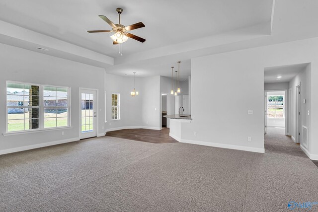 carpeted empty room with ceiling fan with notable chandelier and a tray ceiling