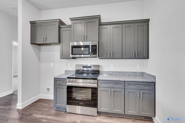 kitchen with stainless steel appliances, baseboards, gray cabinetry, and wood finished floors