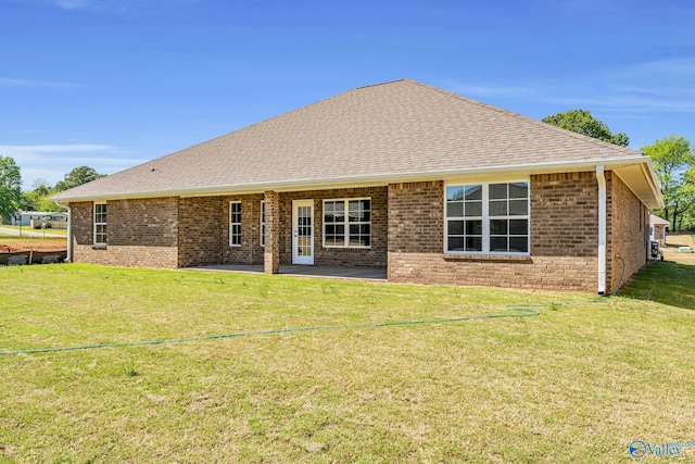 rear view of house with a yard, brick siding, roof with shingles, and a patio area