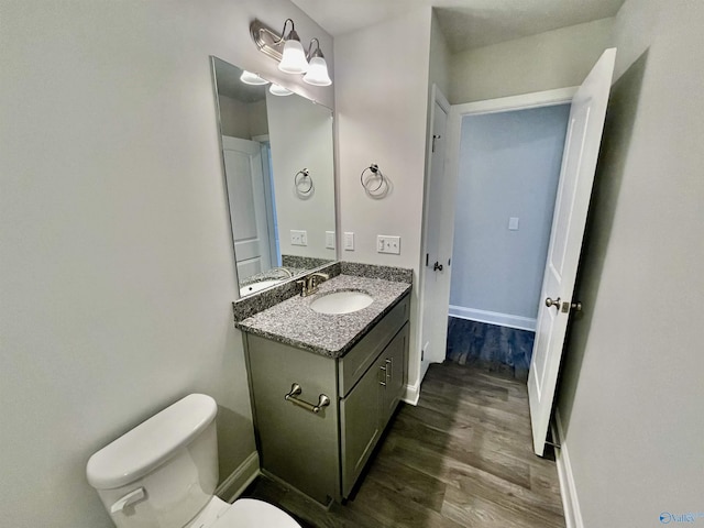 bathroom with toilet, vanity, baseboards, and wood finished floors