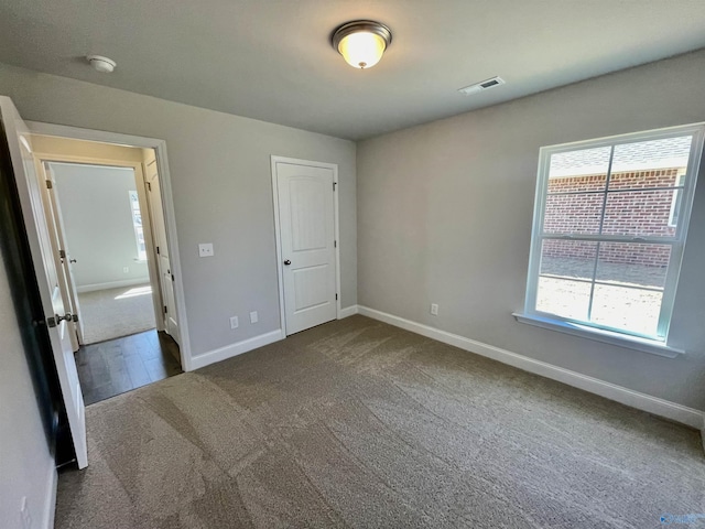 unfurnished bedroom featuring visible vents, multiple windows, baseboards, and dark colored carpet