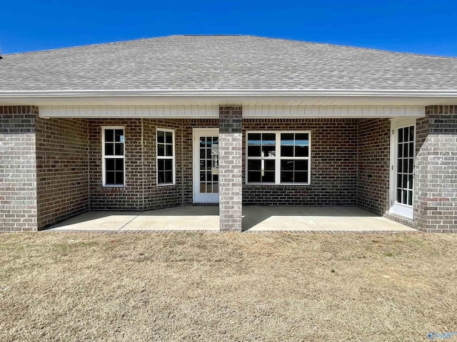 rear view of property with brick siding, a patio area, a shingled roof, and a lawn