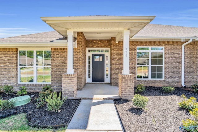 entrance to property with brick siding, covered porch, and roof with shingles