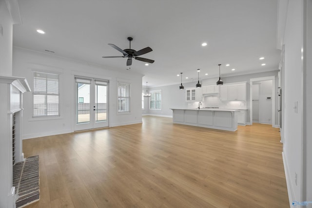 unfurnished living room featuring light wood finished floors, ornamental molding, a brick fireplace, and a wealth of natural light