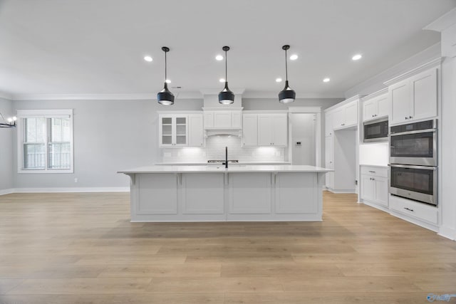 kitchen featuring white cabinetry, black microwave, double oven, pendant lighting, and a kitchen island with sink