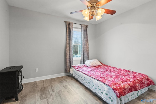 bedroom featuring wood-type flooring, a wood stove, and ceiling fan