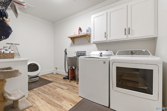 laundry area featuring crown molding, washing machine and clothes dryer, cabinet space, light wood-style floors, and baseboards