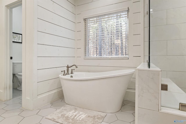 full bath featuring a wealth of natural light, a freestanding tub, tile patterned flooring, and toilet